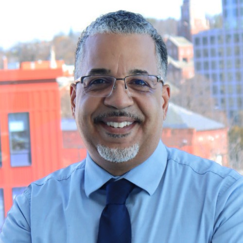 Headshot of Nick Figueroa standing in front of a window overlooking downtown Providence